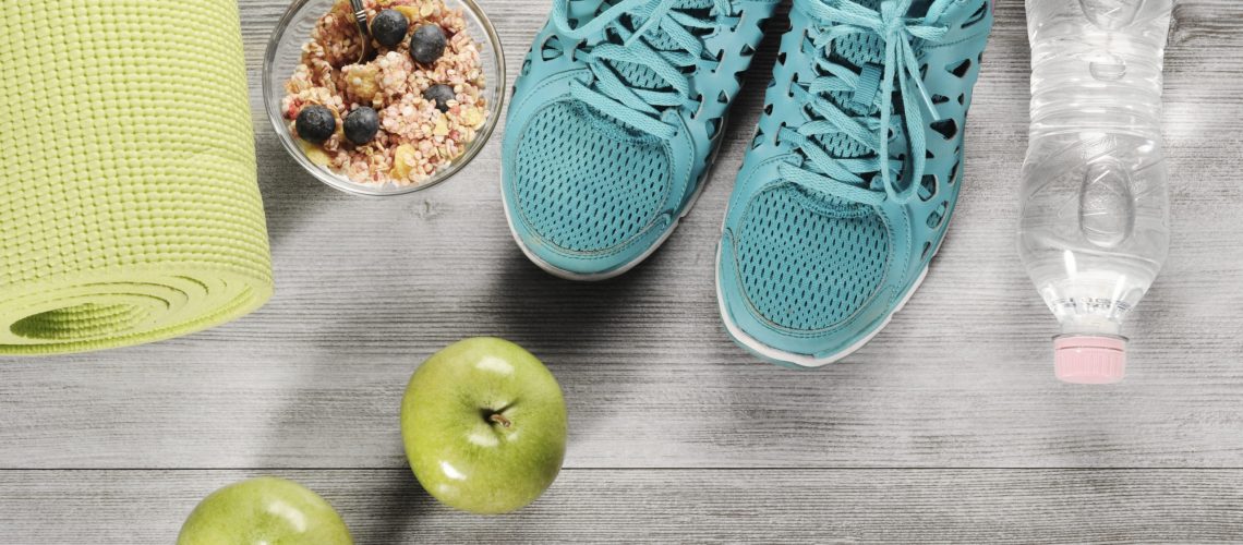 yoga mat with sport shoes and healthy food on a wooden backgroun