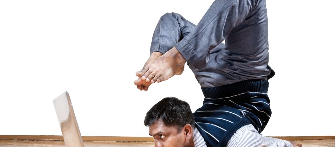 Indian businessman doing yoga and looking at laptop in the office at white background. Free space for your text